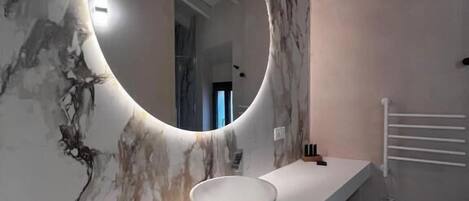 Une salle de bain avec un mur en marbre, un miroir rond et un lavabo blanc.