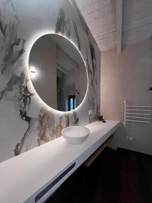 A bathroom with a marble wall, a round mirror, and a white sink.