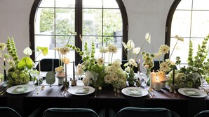 Una mesa de comedor dispuesta con platos, cubiertos y arreglos florales.