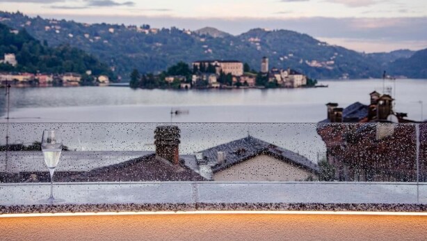 Vista panorámica de un lago con edificios, una copa de vino y cielo despejado.