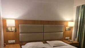 Une chambre d’hôtel avec un grand lit, deux tables de chevet, une tête de lit et deux lampes fixées au mur.