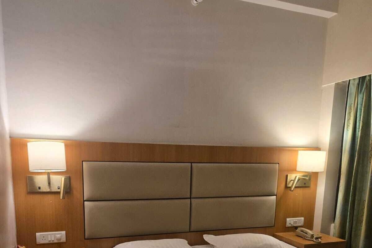 A hotel room with a large bed, two bedside tables, a headboard, and two wall-mounted lamps.
