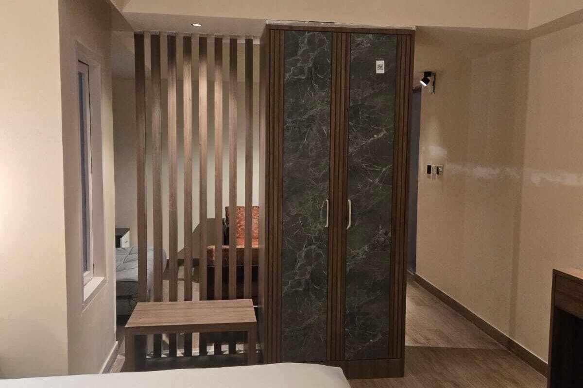 A modern hotel room with a bed, a wooden bench, a sliding door with a marble panel, and a small table.