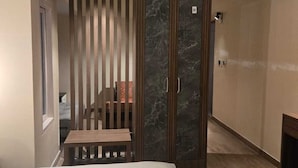 Une chambre d’hôtel moderne comprenant un lit, un banc en bois, une porte coulissante avec un panneau en marbre et une petite table.
