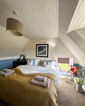 Un dormitorio con cama, lámpara colgante, un cuadro en la pared y ventana con vistas.