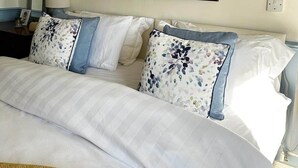 A bedroom with a large bed, a painting above it, and a nightstand with a lamp.