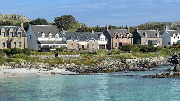 A coastal hotel with multiple buildings, a sandy beach, and clear turquoise waters.