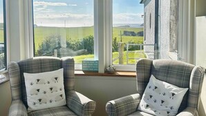 A room with two plaid armchairs, a hanging light fixture, and large windows with a view of a green landscape.