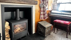 A living room with a fireplace, a television mounted above it, a piano, and a plaid curtain.