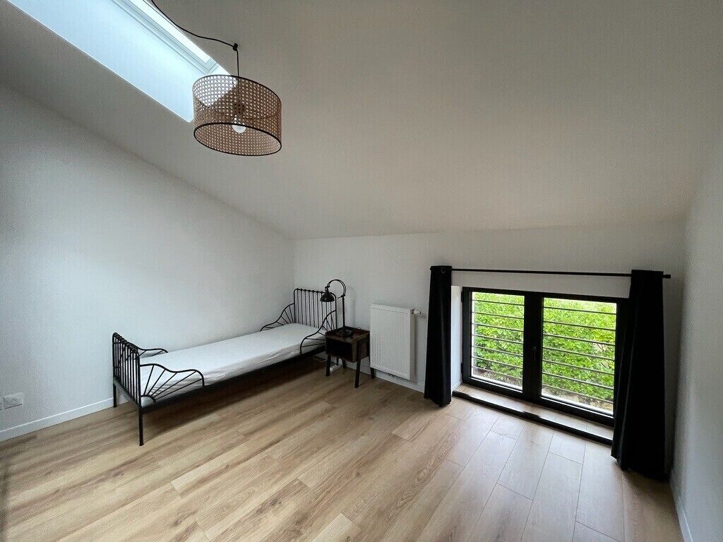 Une chambre avec un lit simple, une petite table, une chaise, un radiateur et une fenêtre donnant sur un espace verdoyant.