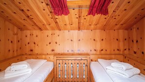 Una habitación de cabaña de madera con dos camas, un cabecero de madera y cortinas rojas.