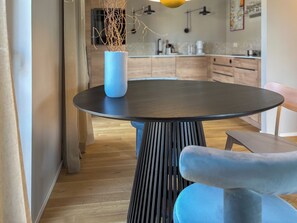 Ein moderner Essbereich mit einem runden Tisch, einer blauen Vase mit Zweigen und einem blauen Stuhl.