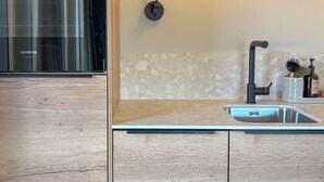 Una cocina moderna con horno empotrado, pileta de acero inoxidable y lámpara fijada a la pared.