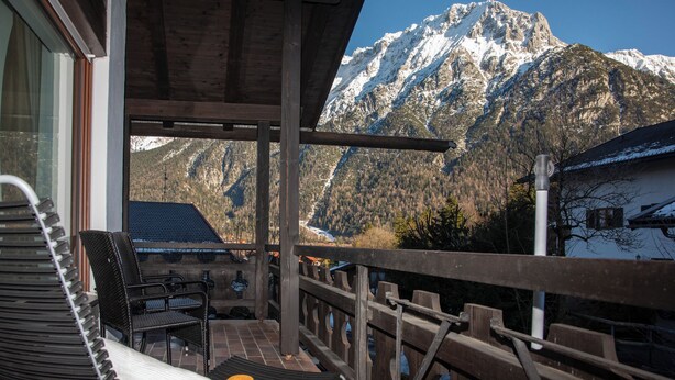 A balcony with a view of snow-capped mountains, a wooden railing, and a chair. - Enchanted forest by Loewenherz (Mittenwald)