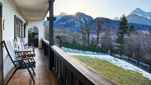 Ein Balkon mit Gartenmöbeln, Blick auf verschneite Berge und ein eingezäunter Garten.