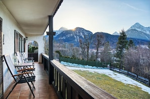 Ein Balkon mit Gartenmöbeln, Blick auf verschneite Berge und ein eingezäunter Garten.