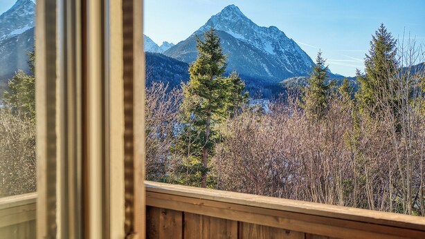Blick auf die Berge vom Holzbalkon mit Fensterrahmen.