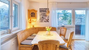 Ein Essbereich mit Holztisch und Bänken, einer Wandleuchte und Blick auf Bäume durch die Fenster.