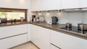 Una cucina moderna con mobili bianchi, un lavandino in acciaio inossidabile, una macchina da caffè e un bollitore.