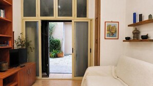 A room with a sofa, a TV on a wooden cabinet, a bookshelf, and a door leading outside. - Loft Of Mirrors In The Center Of Rome (Roma)