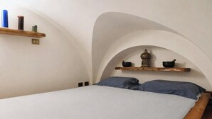 A bedroom with a bed, two pillows, a wooden headboard, and two wooden shelves with decorative items. - Loft Of Mirrors In The Center Of Rome (Roma)