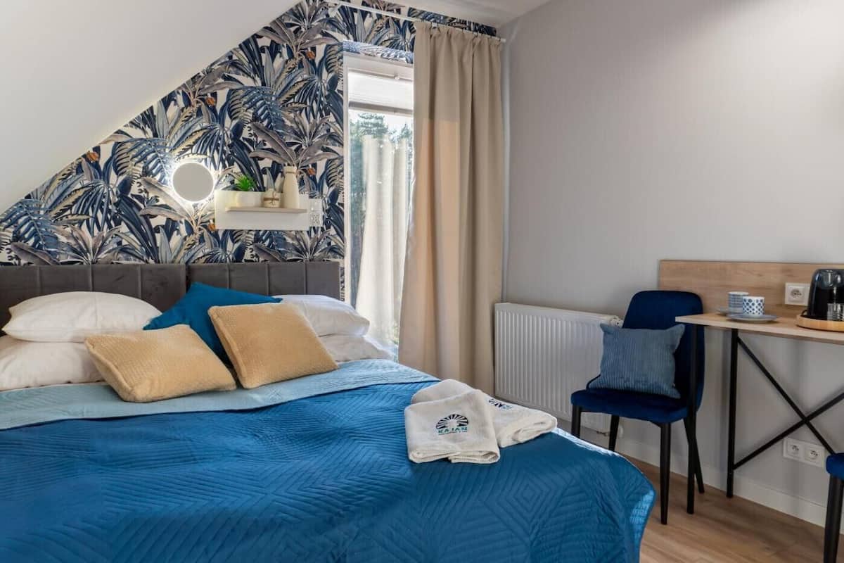 Un dormitorio con cama, escritorio, silla, radiador y ventana con cortinas.