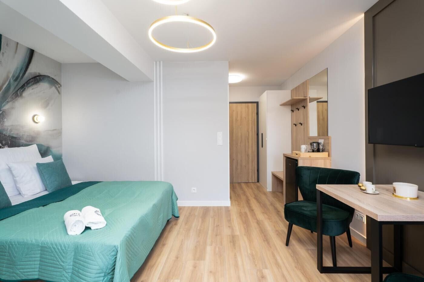 Una habitación de hotel moderna con cama, escritorio, silla, televisor y espejo.