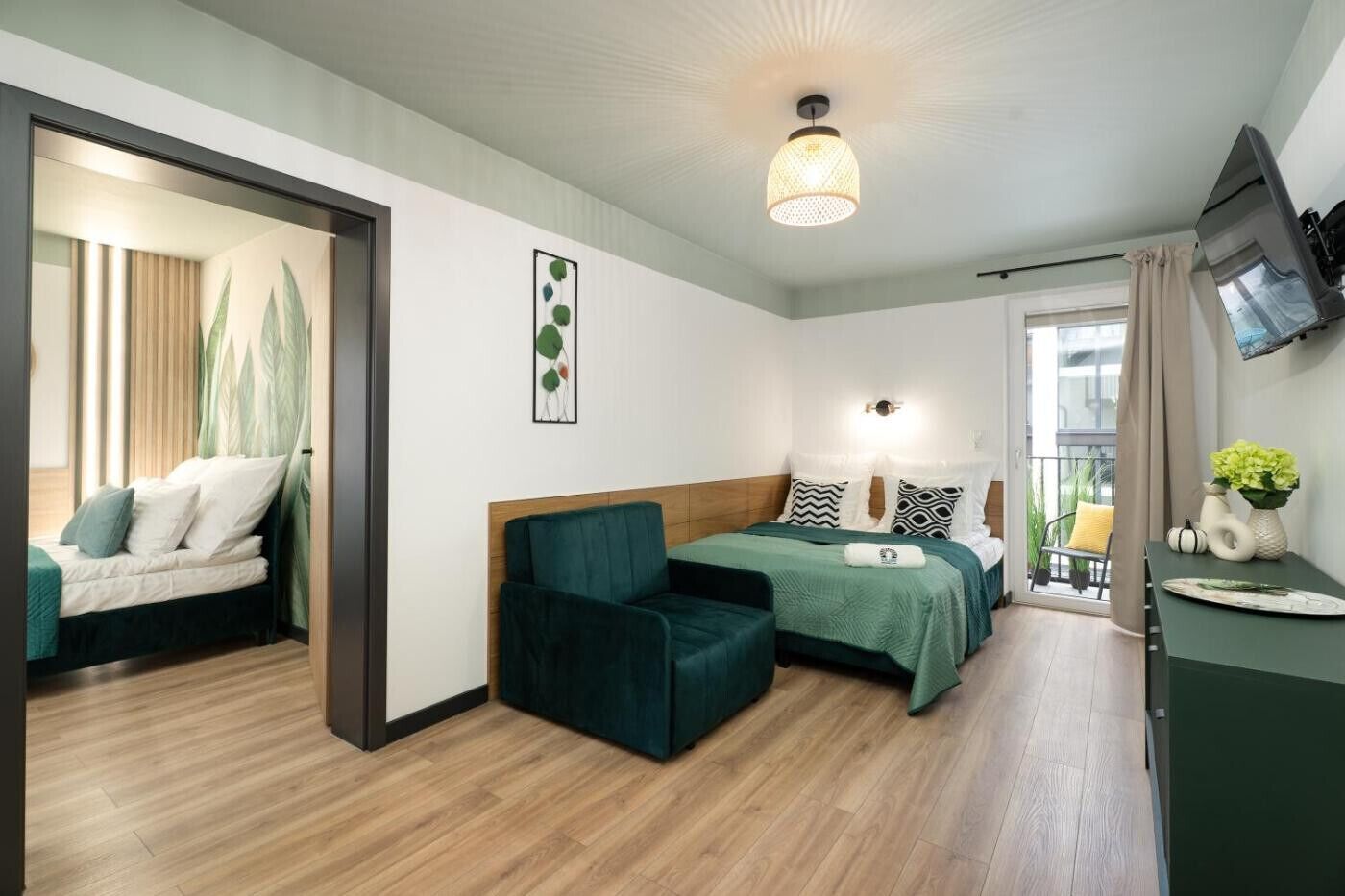 A modern hotel room with a bed, a chair, a desk, and a balcony with plants.