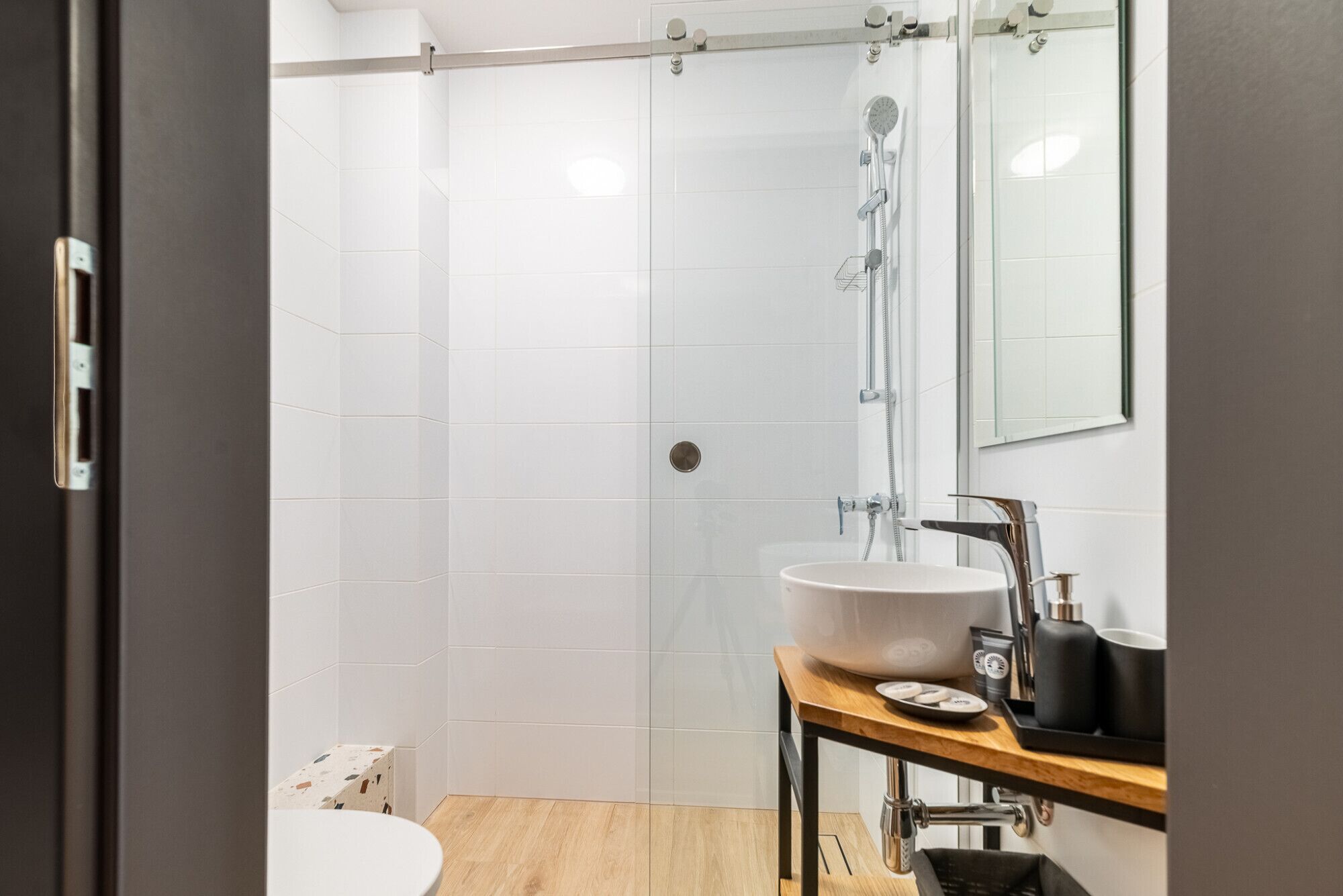 Une salle de bain moderne avec une douche à l’italienne en verre, un lavabo blanc et un meuble-lavabo en bois.