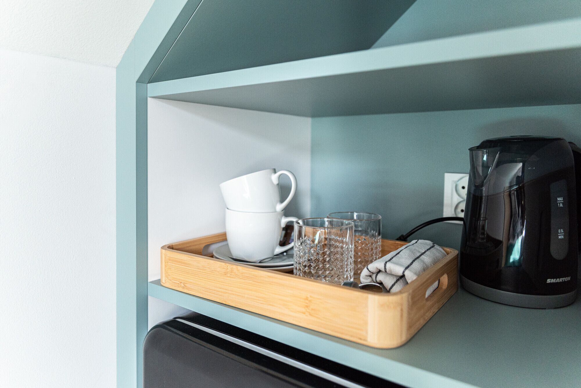 A kitchenette with a coffee maker, a tray with glasses, and a white mug.
