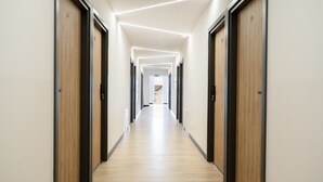 Un corridoio moderno di un hotel con porte in legno, pavimento in legno e illuminazione a incasso.