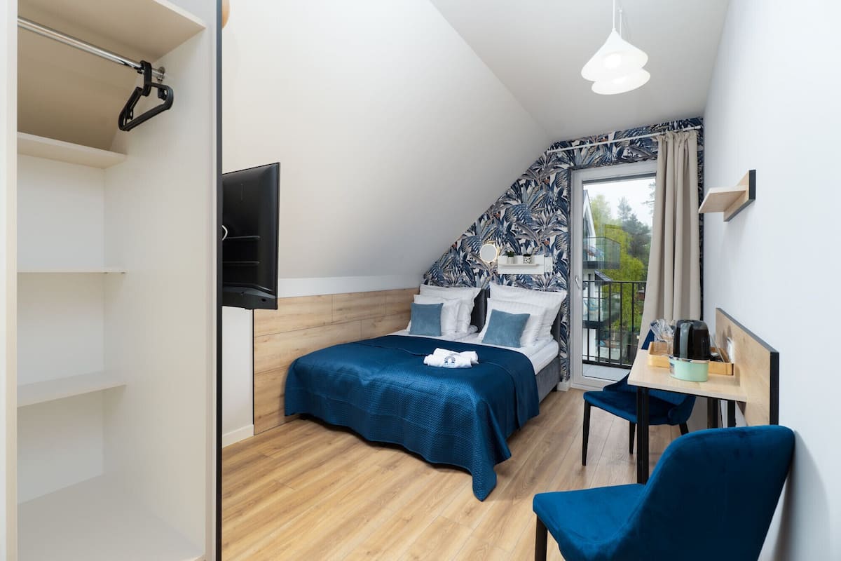 Un dormitorio con cama, escritorio, silla, televisión y balcón con vistas.
