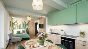 Una cucina moderna con mobili verdi, una zona pranzo con tavolo apparecchiato per due e una camera da letto con un grande affresco floreale.