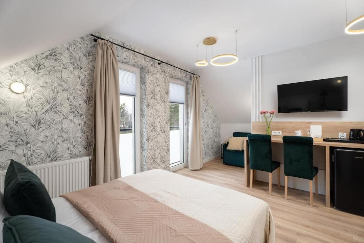 Una habitación de hotel moderna con una cama grande, un escritorio con dos sillas, un televisor de pantalla plana y vistas al exterior.