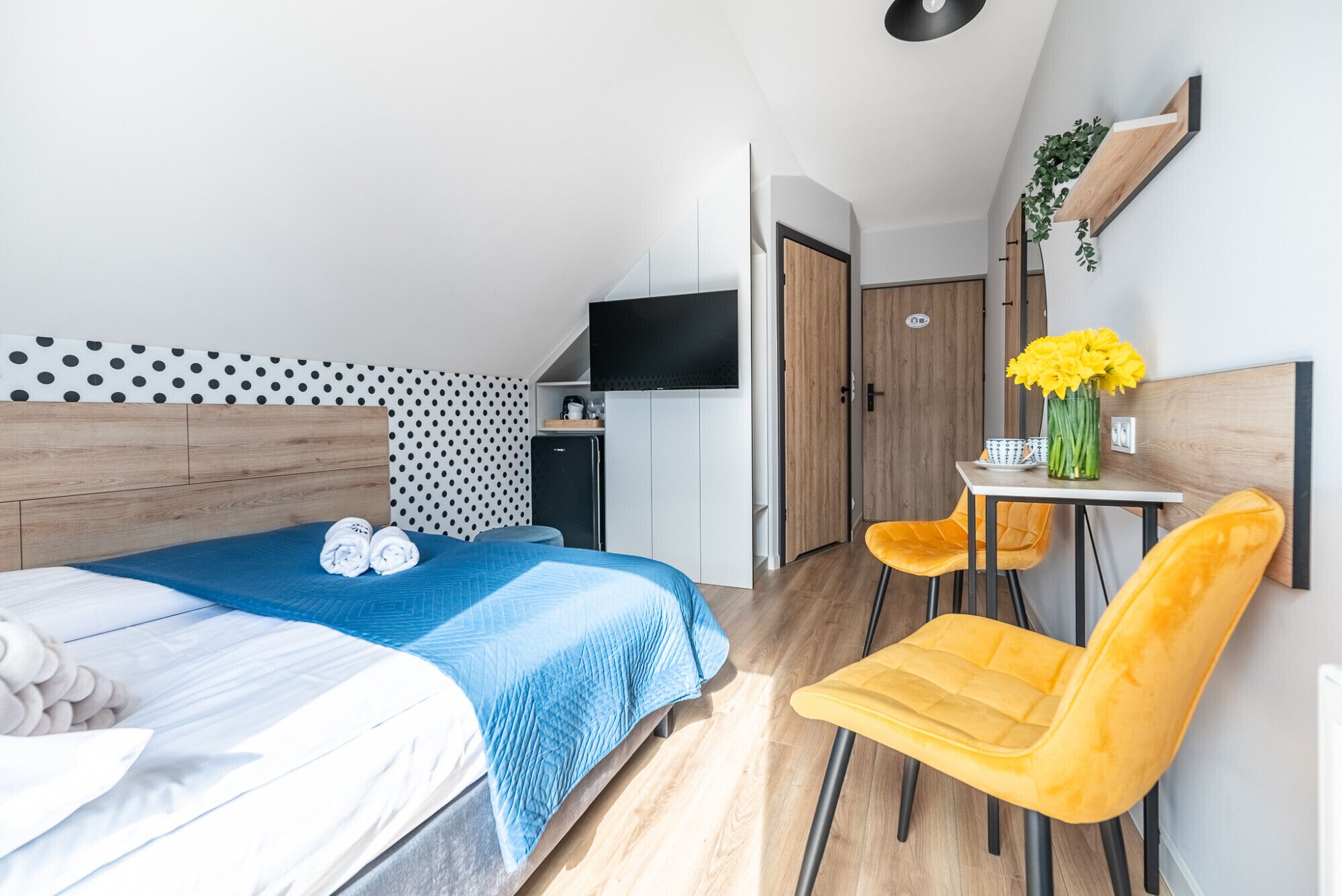 A modern hotel room with a bed, a desk, a chair, and a TV.