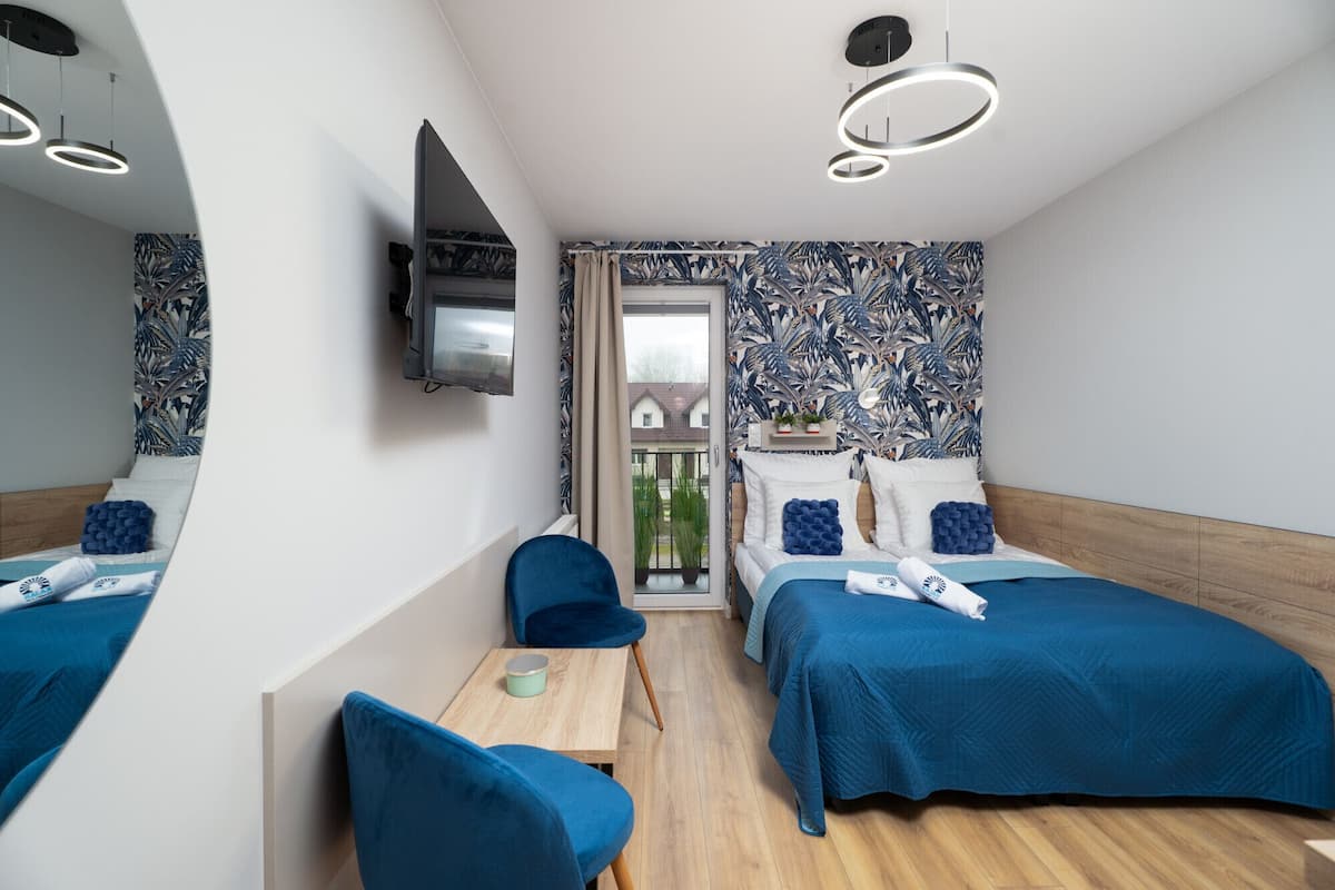 Una habitación de hotel moderna con dos camas, televisor, una mesita pequeña y un balcón con vistas.