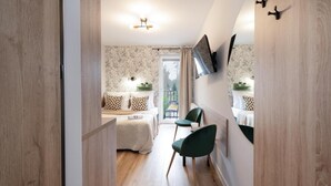 Una camera d'albergo moderna con pavimento in legno, un letto con biancheria bianca, una sedia verde, una TV a muro e un balcone con vista.