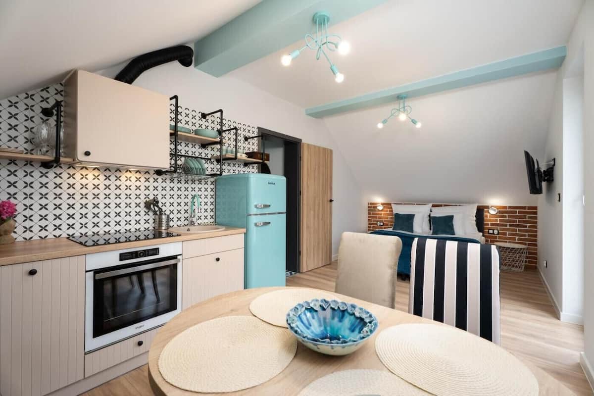 Una cocina compacta con una estufa moderna, un refrigerador azul y un comedor con una mesa redonda y sillas.