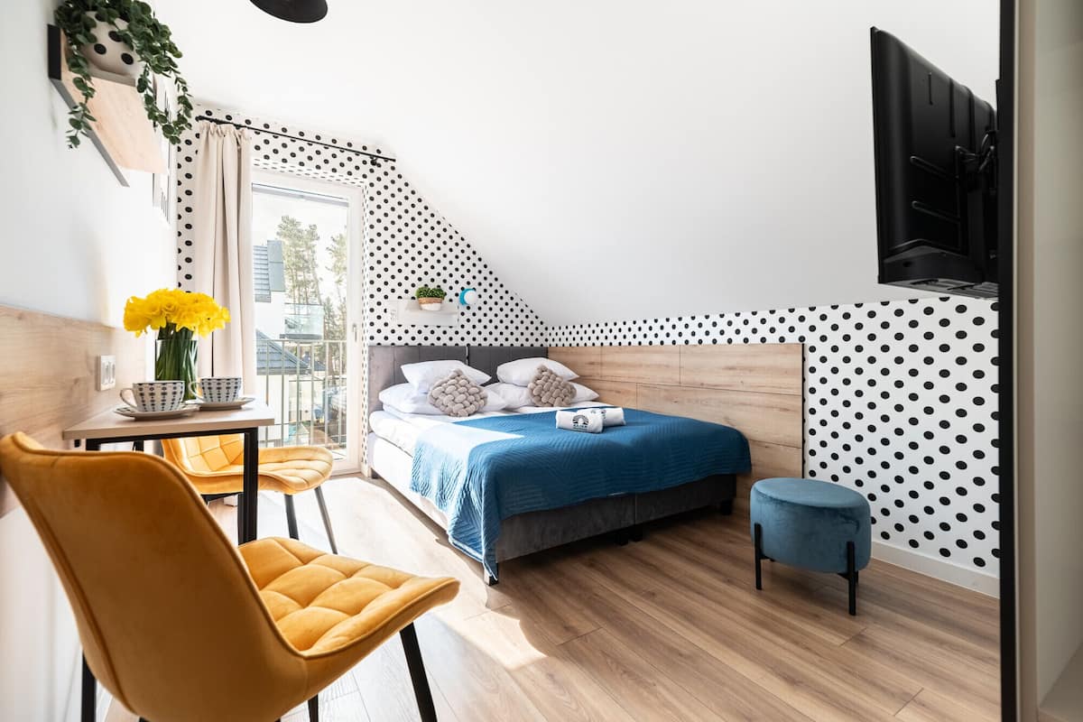 Un dormitorio con cama, escritorio, silla, una pequeña mesa con flores y una planta en maceta.