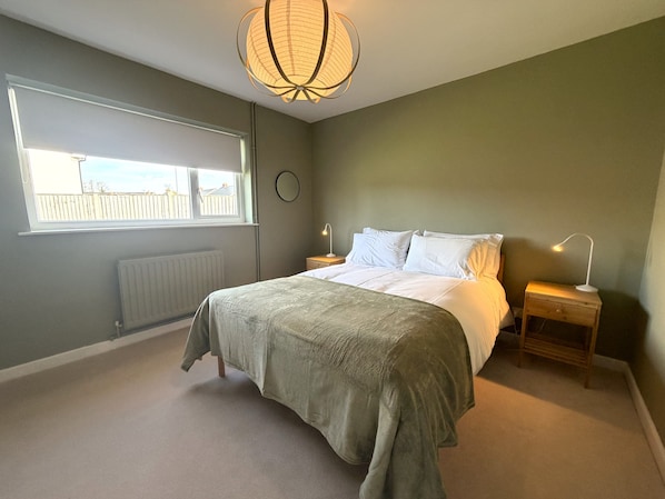 A bedroom with a bed, bedside tables, a window, a radiator, and a ceiling light fixture.