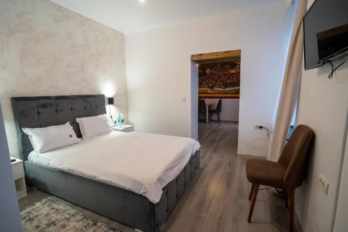Un dormitorio con cama, mesita de noche, silla y televisor montado en la pared.