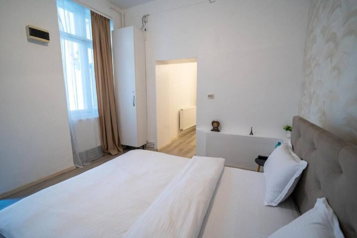 Habitación de hotel con cama, mesita de noche, lámpara y vista al pasillo.