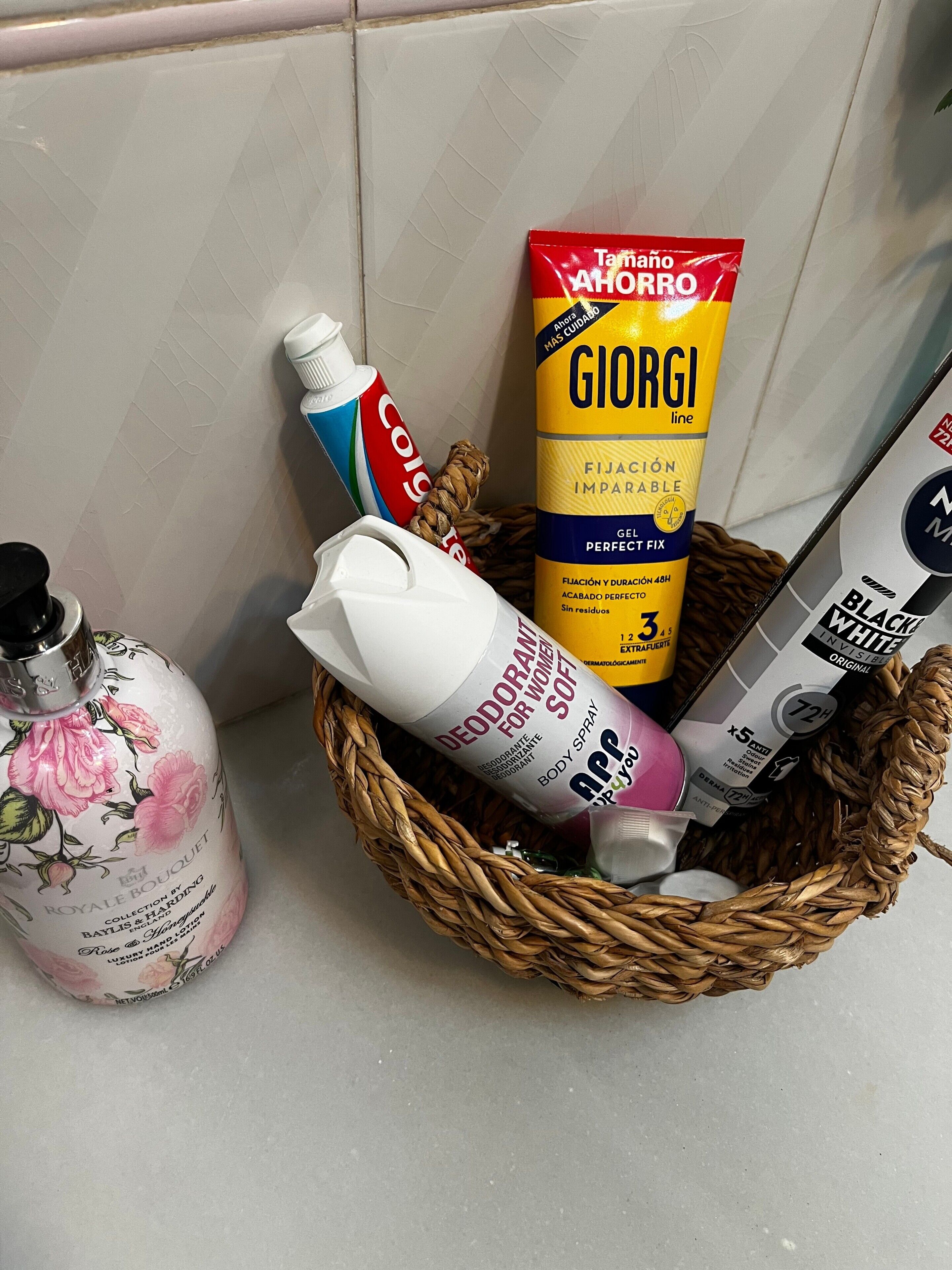 Una cesta de mimbre con diversos artículos de tocador, incluyendo un envase de desodorante, un tubo de aerosol corporal, una lata de espuma de afeitar y una caja de gel de afeitar.