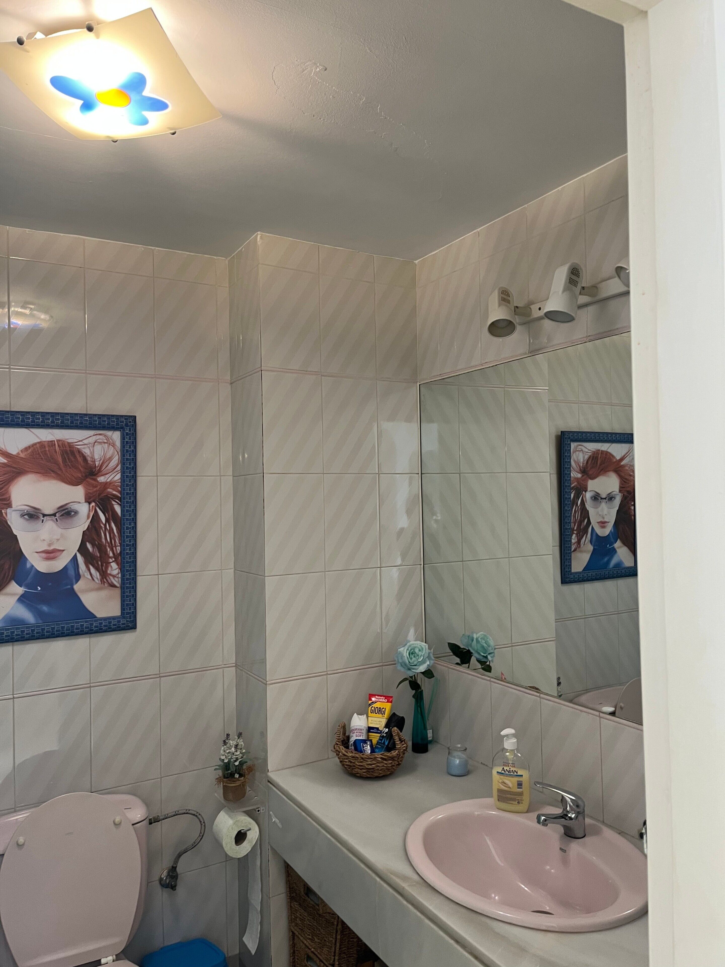 A bathroom with a toilet, sink, mirror, and tiled walls.