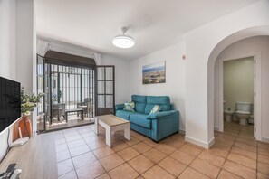 A living room with a sofa, a coffee table, a TV, and a door leading to a balcony. - Apartment 'El Molino Del Viento' with Private Terrace, Wi-Fi and Air Conditioning (Conil de la Frontera)