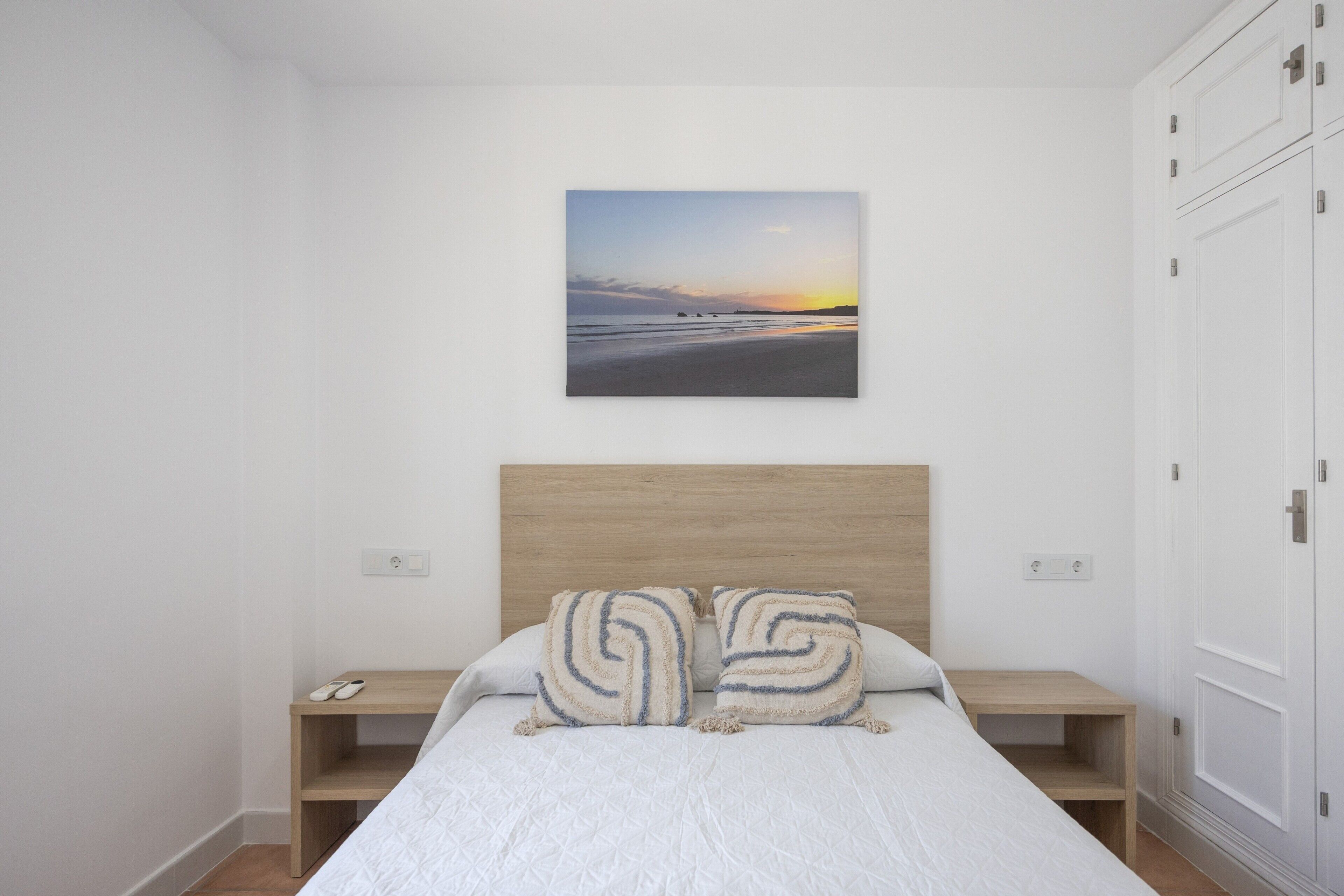 Een slaapkamer met een bed, twee nachtkastjes, een hoofdeinde en een aan de muur bevestigd schilderij.
