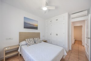 A bedroom with a bed, a nightstand, a ceiling fan, a wardrobe, and a painting on the wall. - Apartment 'El Molino Del Viento' with Private Terrace, Wi-Fi and Air Conditioning (Conil de la Frontera)