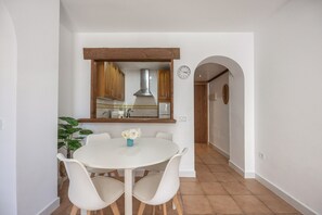 Ein Essbereich mit einem weißen Tisch und Stühlen, einer Zimmerpflanze und einer Küche im Hintergrund.