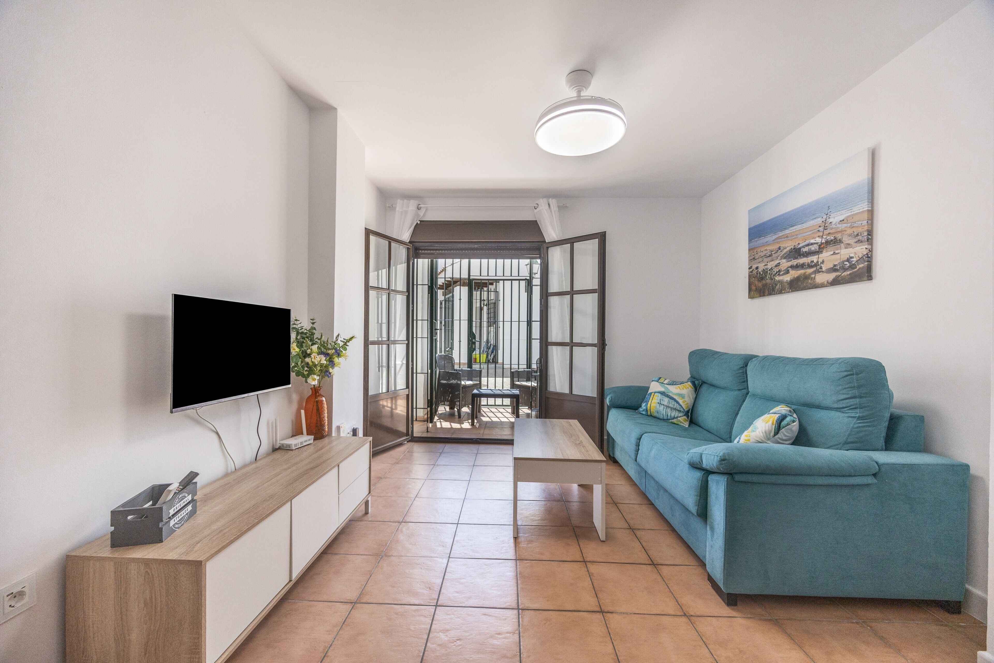 Een moderne woonkamer met een flatscreen televisie, een blauwe bank, een houten salontafel en uitzicht door een glazen deur op een buitengebied.