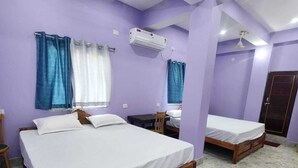 A room with two beds, a table, a chair, an air conditioning unit, and a ceiling fan. - Hotel Navin Palace (Bhagalpur)